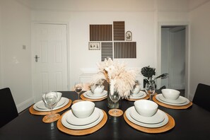 A dining table set with white plates, bowls, and glasses, accompanied by a vase with dried flowers. - Central Warrington 2-Bed Home near Hospital & Train Station | Free Parking (Warrington)