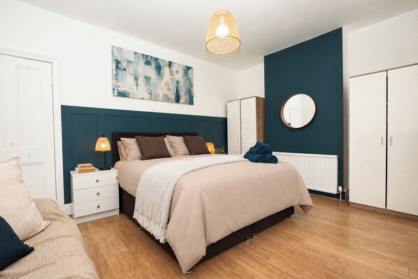 A bedroom with a bed, bedside tables, a wardrobe, a radiator, and a painting on the wall. - Central Warrington 2-Bed Home near Hospital & Train Station | Free Parking (Warrington)