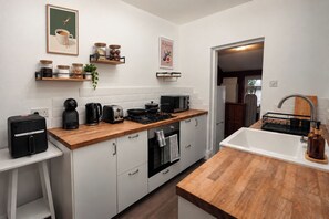 Eine moderne Küche mit weißen Schränken, einer Holzarbeitsplatte, einem eingebauten Backofen, einer Mikrowelle, einer Kaffeemaschine und einem Toaster. Außerdem sind Regale mit Gläsern und eine Pflanze zu sehen.