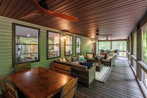 A covered porch with wooden flooring, green walls, wicker furniture, and large windows. - The Crooked Tree-a peaceful mountain home in The New River Gorge National Park (Fayetteville)