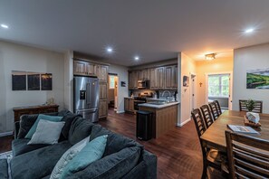A modern kitchen with stainless steel appliances, wooden cabinets, and a dining area with a table and chairs. - The Crooked Tree-a peaceful mountain home in The New River Gorge National Park (Fayetteville)