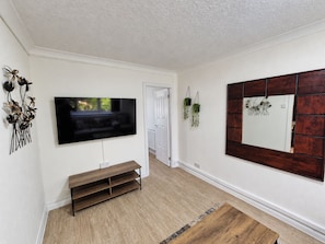 Ein Zimmer mit einem wandmontierten Flachbildfernseher, einer Holzbank, einem großen Spiegel und zwei hängenden Pflanzgefäßen.