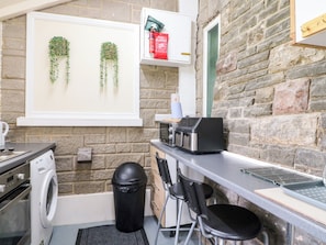 A compact kitchen with a washing machine, a trash bin, and a small bar area with a toaster. - Greystones - C (Buxton)