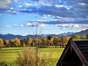 Ländliche Landschaft mit blauem Himmel, Bergen im Hintergrund und einem Gebäude mit geneigtem Dach.