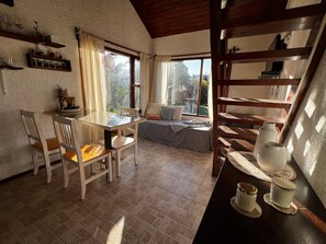 A cozy room with a dining table, chairs, a sofa, and a window with curtains. - Depto. con vista al Huapi a 200 m de Playa Bonita (San Carlos de Bariloche)