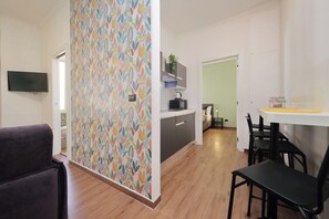 A modern kitchen with a dining area, a flat-screen TV mounted on the wall, and a patterned wallpaper. - 4BNB - Eroi Vatican Apartment (Rome)