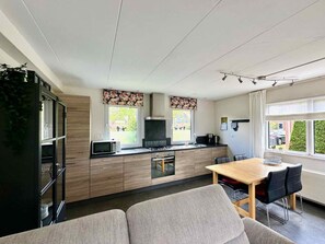 A modern kitchen with a dining area, featuring a built-in microwave, stove, and cabinets. - Holiday Home With 2 Bedrooms (Oostkapelle)