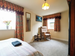 A hotel room with a bed, a chair, a small table, a mirror, and a window with curtains. - Greystones -D (Buxton)