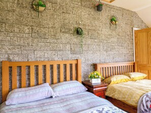 Ein Schlafzimmer mit zwei hölzernen Betten, einer Steinwand und hängenden Pflanzen.