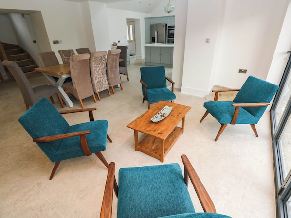 A living room with teal chairs, a wooden coffee table, and a dining area with patterned chairs. - Mariners Way (Narberth)