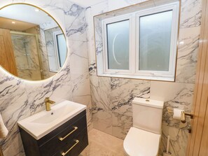 A bathroom with a marble wall, a round mirror, a toilet, and a sink with a gold faucet. - Mariners Way (Narberth)