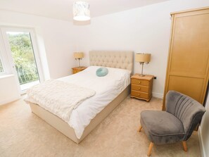 A bedroom with a large bed, bedside tables, a chair, a wardrobe, and a window with a view. - Mariners Way (Narberth)