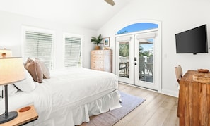 Ein Schlafzimmer mit Bett, Kommode, Fernseher und Blick ins Freie durch eine Glasdoor.
