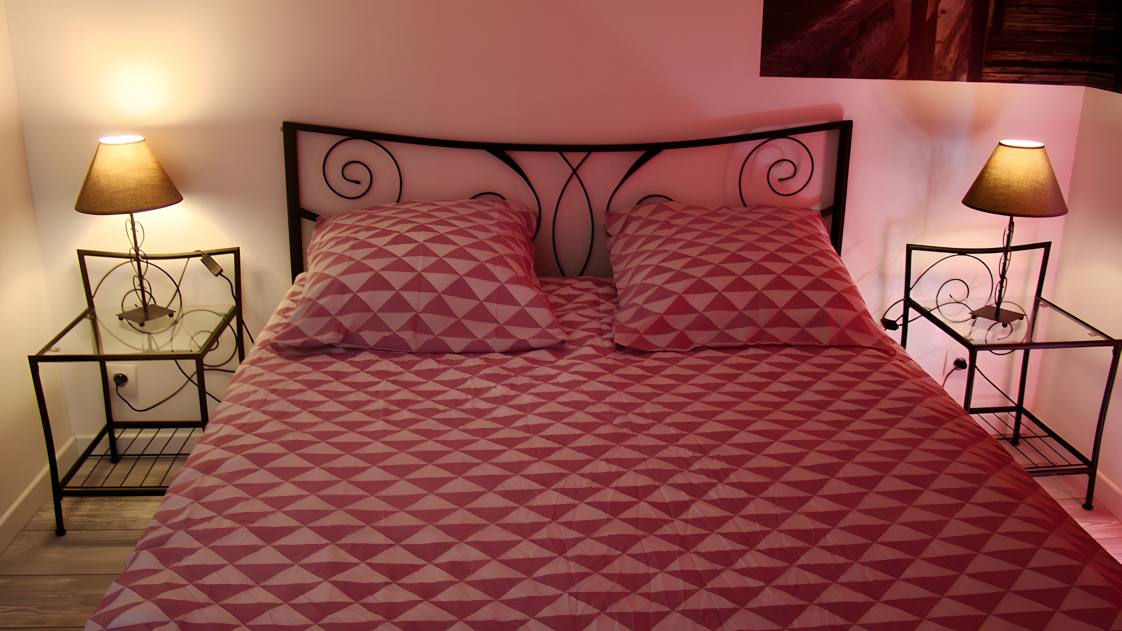 A bed with a geometric patterned bedspread, two bedside tables with lamps, and a metal headboard.