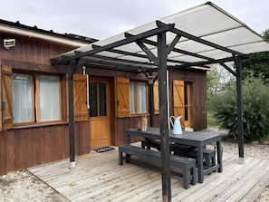 Uma cabana de madeira com varanda coberta, um banco e um vaso com planta.
