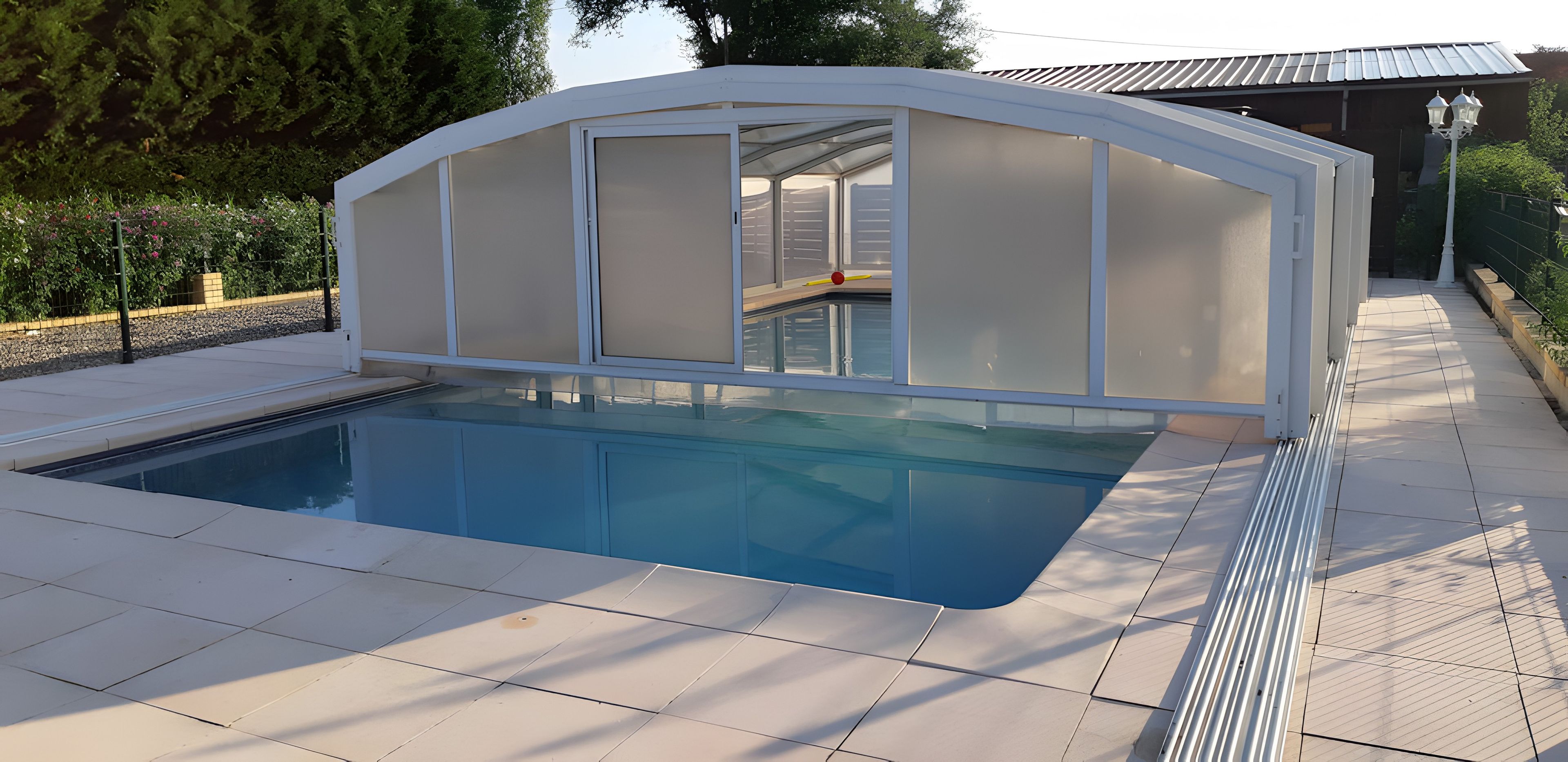Una piscina con cerramiento de vidrio y solárium de baldosas.