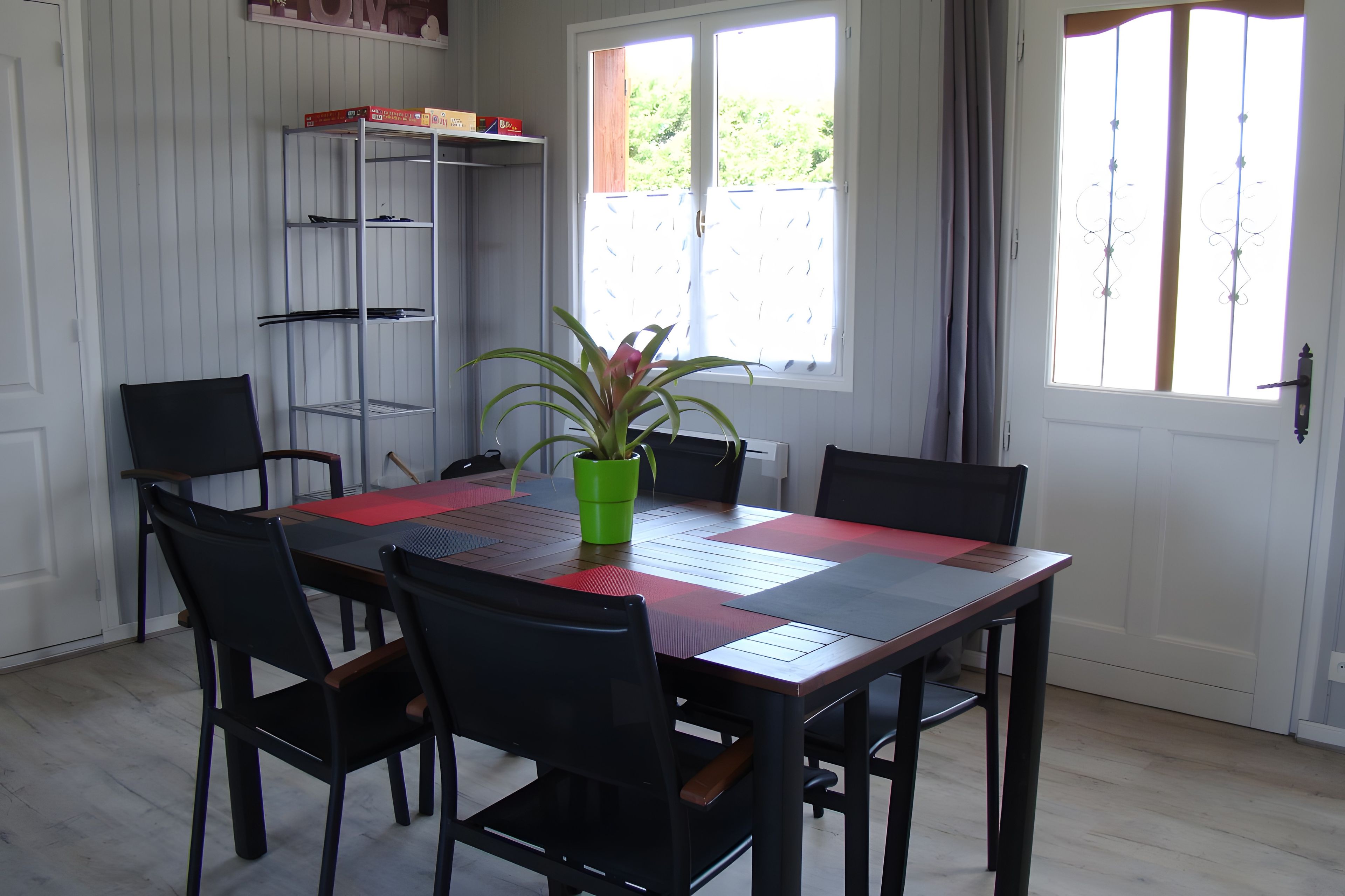 Een eetruimte met een tafel gedekt voor zes personen, omringd door stoelen, een potplant en een metalen wandplank.