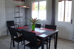 Een eetruimte met een tafel gedekt voor zes personen, omringd door stoelen, een potplant en een metalen wandplank.