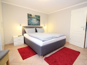 A bedroom with a bed, nightstands, a painting, and a red rug. - Holiday Apartment in Sylt With 3 Bedrooms (Sylt)