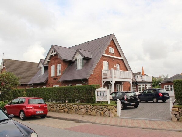 A two-story brick building with a sloped roof, a balcony, and a stone wall. - Holiday Apartment in Sylt With 3 Bedrooms (Sylt)