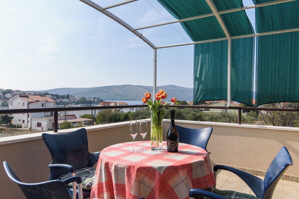 Een balkon met een tafel gedekt voor twee personen, een fles wijn en een vaas met bloemen.