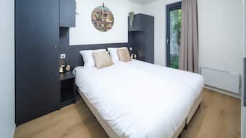 Ein modernes Schlafzimmer mit einem großen Bett, dunklen Schränken, einer Wandpflanze und einem Fenster mit Vorhängen.