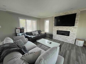 Una sala de estar con un sofá gris, una mesa de centro, un televisor de pantalla plana montado en una pared de piedra y una chimenea.