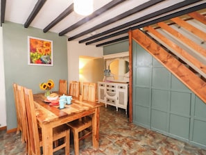 A dining area with a wooden table and chairs, a vase of sunflowers, and a painting on the wall. - Ty Driffter (Porthmadog)