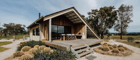 Ein modernes Holzhaus mit einer Terrasse, großen Fenstern und einer Schotterauffahrt.