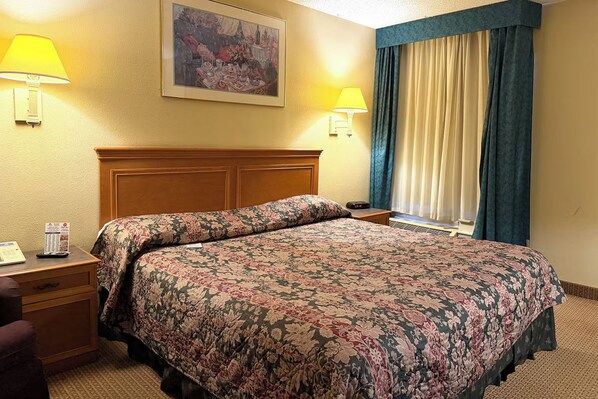 A hotel room with a bed, bedside lamps, a desk with a telephone, and a window with curtains.
