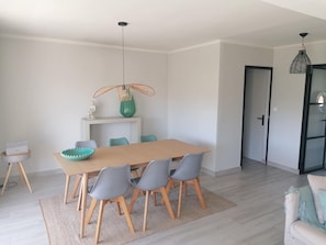 Ein moderner Essbereich mit einem Holztisch und grauen Stühlen, einem kleinen Beistelltisch mit einer Schüssel und einer hängenden Leuchte.