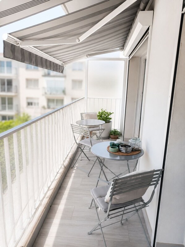 Ein Balkon mit Tisch und Stühlen, einem Blumentopf und Blick auf Gebäude im Hintergrund.