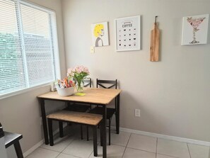 Un comedor con mesa de madera, sillas, un florero con flores y decoración de pared que incluye una guía de café y un vaso de martini.