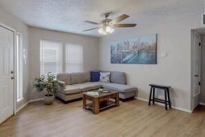 Ein Wohnzimmer mit Sofa, Couchtisch, Deckenventilator, einem Gemälde und einer Topfpflanze.
