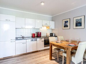 A modern kitchen with white cabinets, a wooden dining table, and two framed pictures on the wall. - Zeuke Holiday Apartment Klunderberg (Binz)