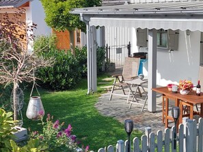 Ein Garten mit einem Holztisch, Stühlen und einem weißen Zaun.