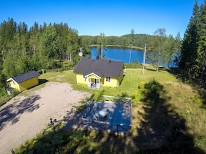 Ein gelbes Haus mit einer Terrasse, umgeben von Wald und See.