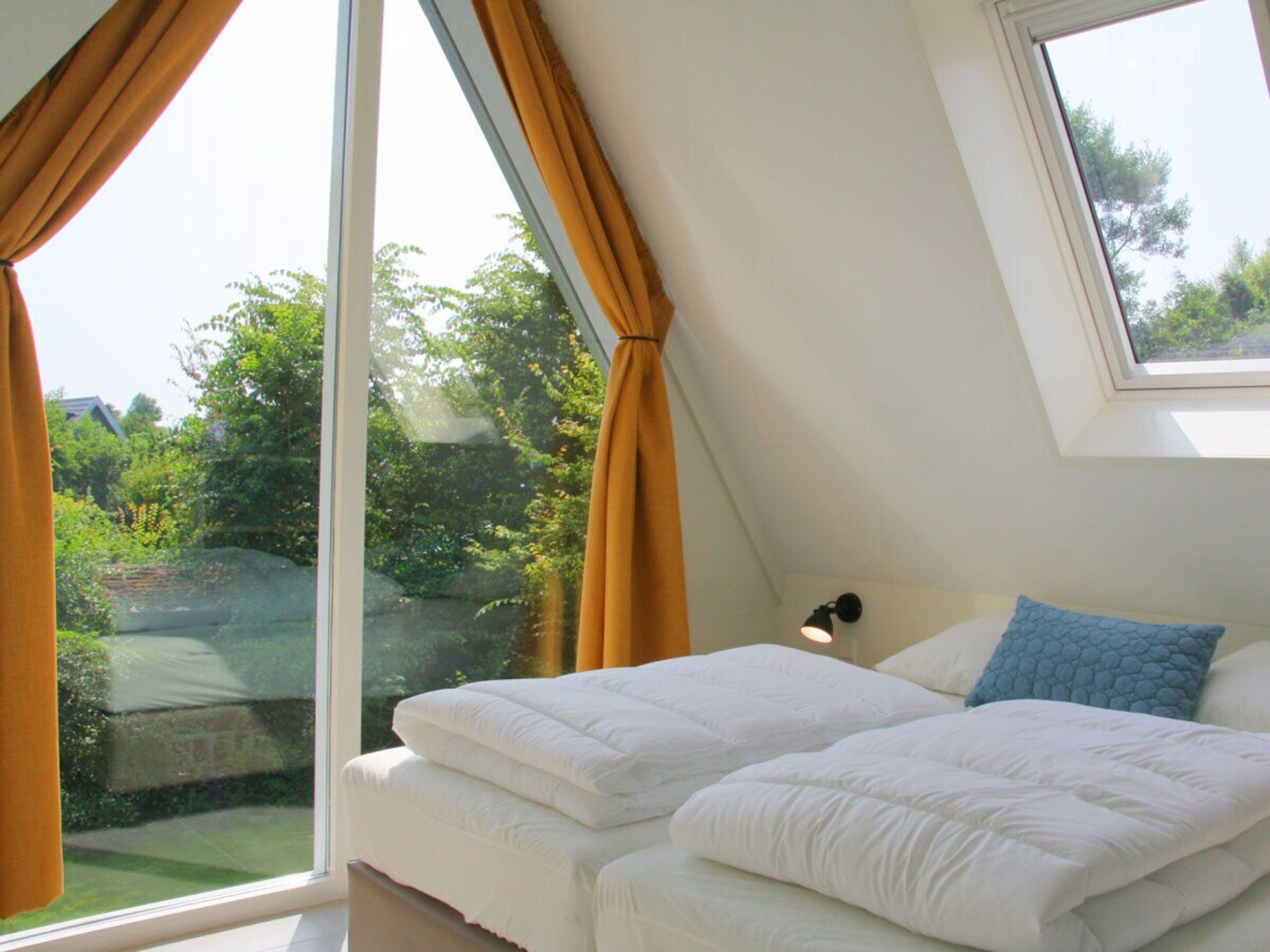 A bedroom with a bed, a window with curtains, a skylight, and a view of greenery outside.
