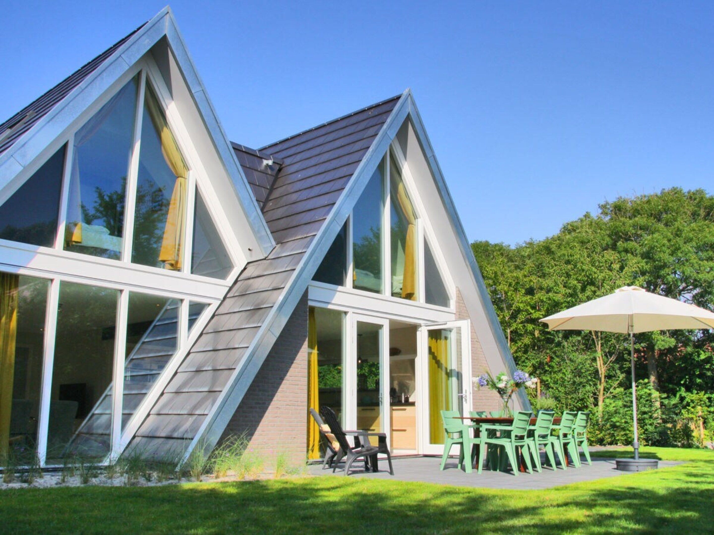 A modern house with a sloped roof, large windows, and a patio with outdoor furniture.