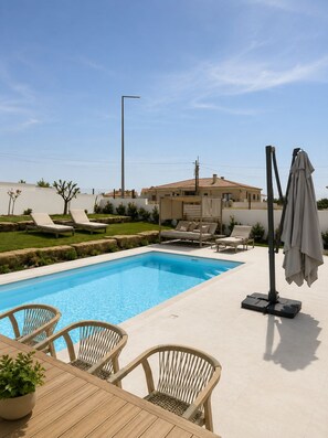 A swimming pool with lounge chairs and a table, surrounded by a landscaped garden and a building with a tiled roof. - Casa Onda - Spa House & Ocean-View Jacuzzi (Atouguia da Baleia)