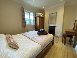 A bedroom with a bed, a chair, a fireplace, and a window with curtains. - Rivercrest (Looe)