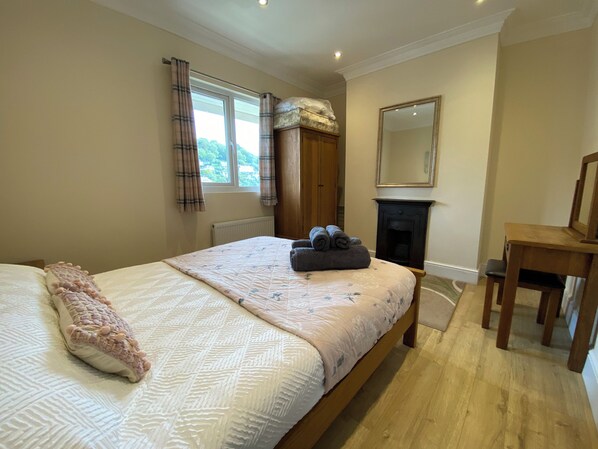 A bedroom with a bed, a chair, a fireplace, and a window with curtains. - Rivercrest (Looe)