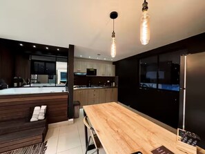 A modern kitchen with wooden cabinets, a large wooden table, and pendant lighting. - Oasis Loft Friends (Medellín)