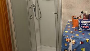 A shower enclosure with a glass door, a handheld showerhead, and a shelf with toiletries.