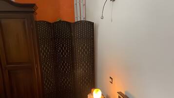 Un dormitorio con una cama que presenta un diseño con cielo y nubes, un armario de madera, una mesita de noche con lámpara y un aplique de pared.