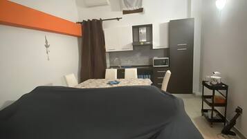 A hotel room with a bed, a small kitchenette, a dining table, and a single chair.
