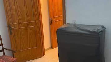 A room with a bed, a chair, a large suitcase, and a wooden door.