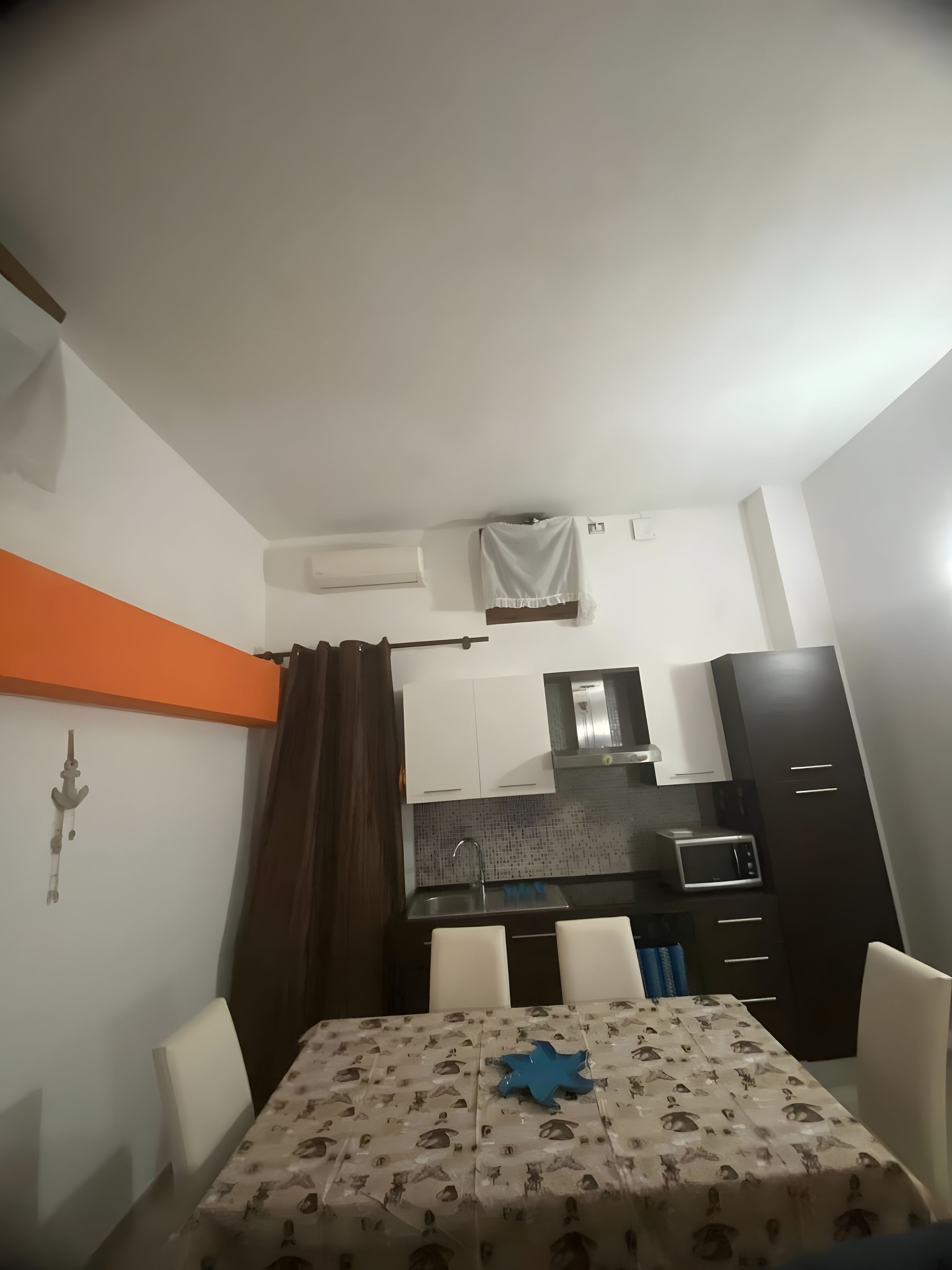 Une cuisine compacte équipée d’un four à micro-ondes, d’un évier et de placards, un coin repas avec une table et des chaises, et un rideau de douche.