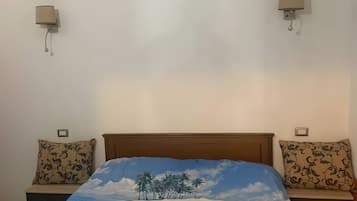 Een slaapkamer met een bed met een tropisch stranddesign, twee nachtkastjes met lampen en een houten hoofdbord.