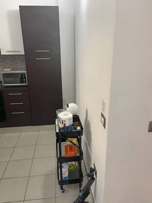 Eine Küche mit einer Mikrowelle, dunklen Schränken, einem kleinen Wagen mit Küchenutensilien und einer weißen Wand.